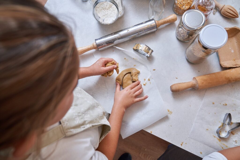 From above of crop unrecognizable kid making homemade cookies with cutter from dough rolled out on table