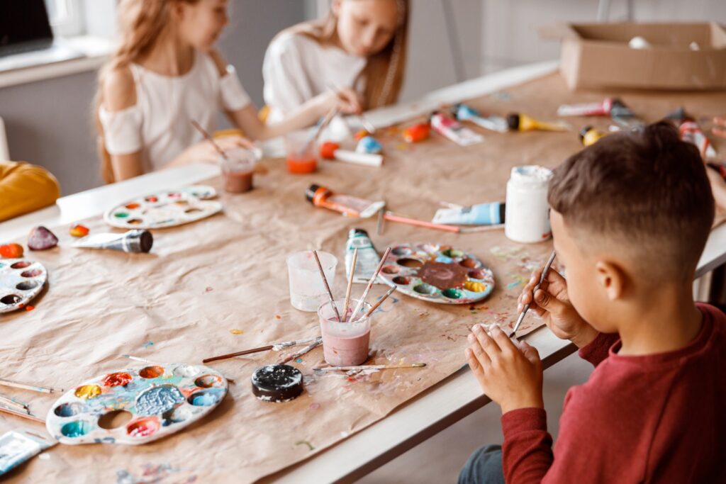 Happy little boy sitting at the table while drawing with watercolor together with his classmates. Education concept